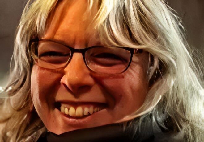 Cheerful person with long hair and glasses.